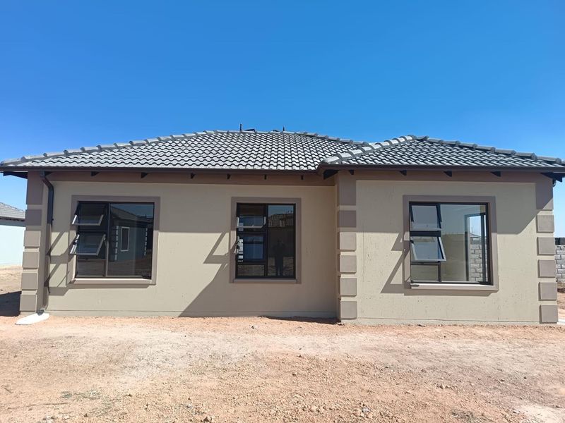 A view of the rear elevation of a modern house featuring a tiled roof, plastered walls with corner detailing, and dark aluminium top-hung windows.