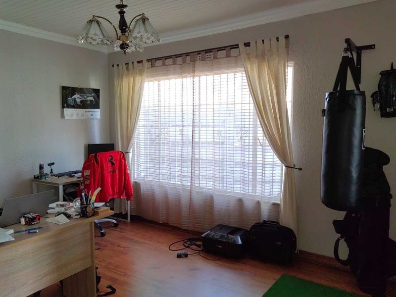 A functional home office space featuring laminate flooring, a beaded ceiling with decorative coving, and a large window with security bars.