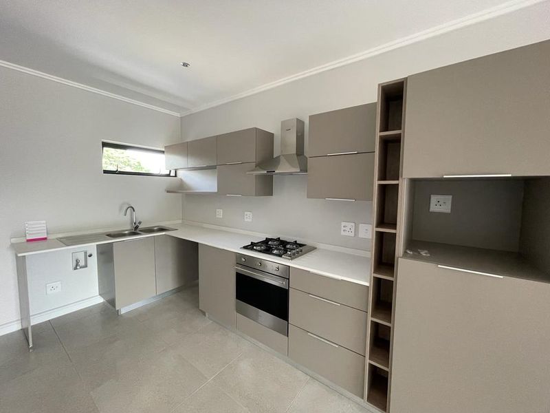 Modern kitchen featuring neutral-toned built-in cabinetry, stone countertops, stainless steel gas hob, oven, extractor fan, and tiled flooring.