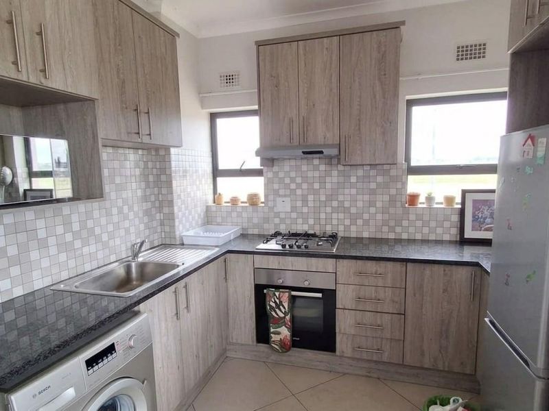 A functional kitchen featuring wood-look cabinetry, granite countertops, a mosaic tile backsplash, and integrated appliances including a gas hob and oven.