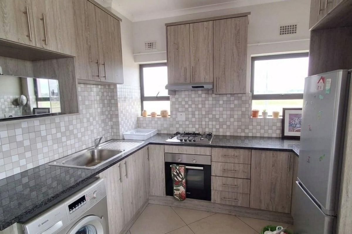A functional kitchen featuring wood-look cabinetry, granite countertops, a mosaic tile backsplash, and integrated appliances including a gas hob and oven.