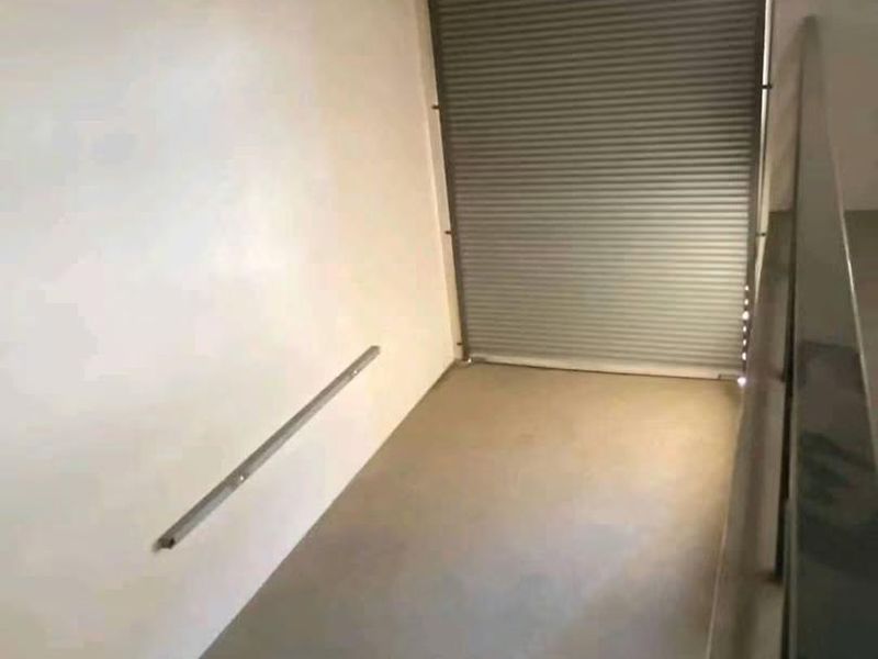A clean, empty utility space featuring concrete flooring, a secure roller shutter door, and a metal handrail, suitable for storage or functional use.