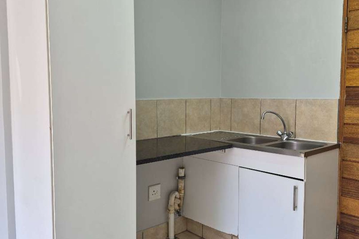 A compact kitchen area featuring built-in cabinetry, a stainless steel sink, tiled backsplash, and tiled flooring, currently in need of minor cosmetic updates.