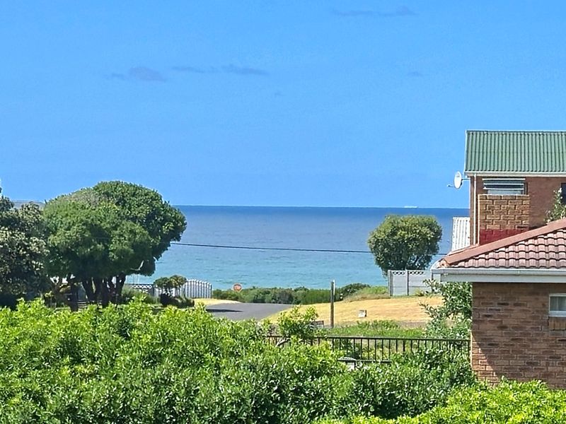 A scenic view of the ocean horizon captured from an elevated position, featuring surrounding residential brick architecture and mature greenery.