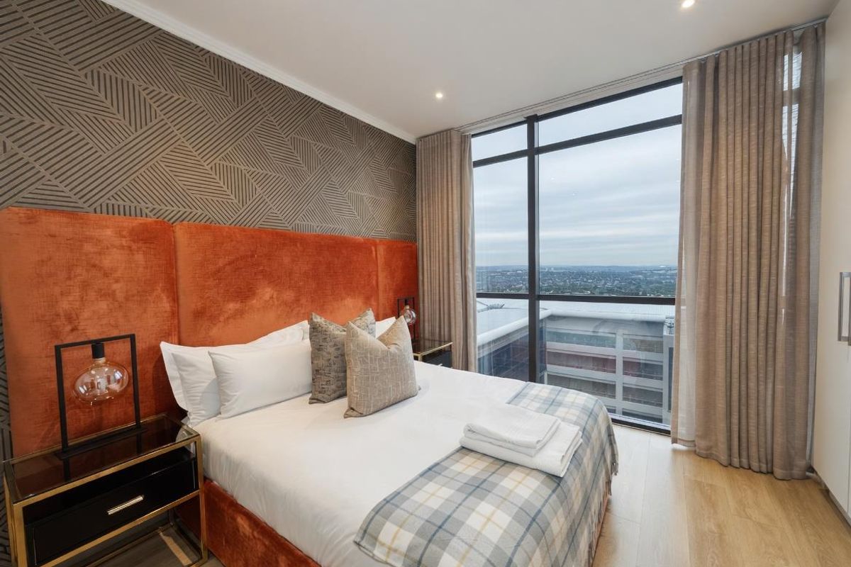 Modern bedroom featuring floor-to-ceiling windows with expansive city views, wood-look flooring, and recessed downlighting.