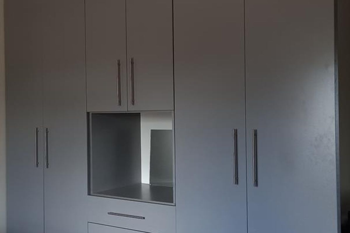 A modern bedroom featuring floor-to-ceiling built-in cabinetry with integrated drawers and a central open display niche.