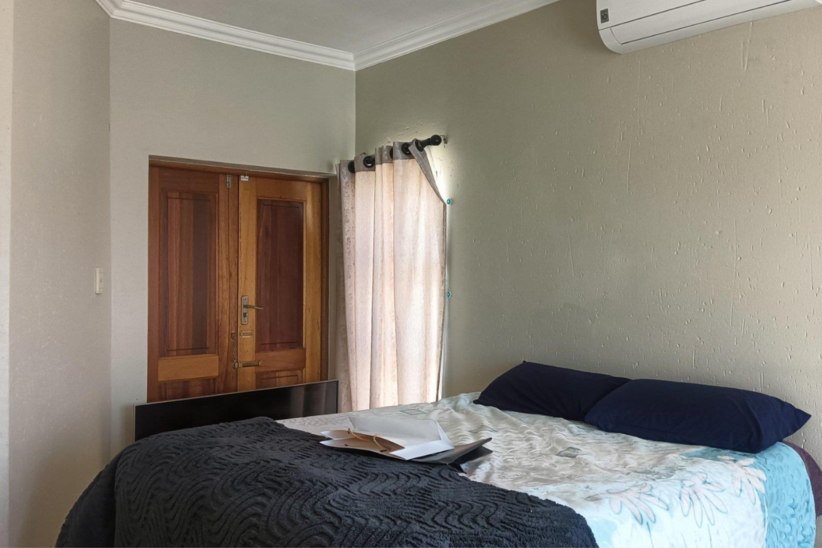 A bedroom featuring a wall-mounted air conditioning unit, wooden double doors, and neutral wall finishes.