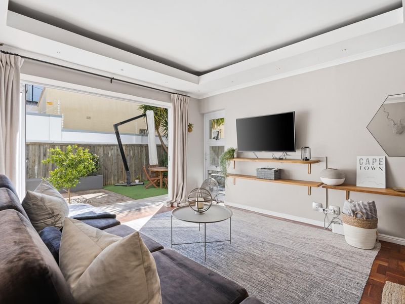 Bright living room featuring parquet flooring, recessed ceiling lighting, and large sliding glass doors opening onto a private outdoor patio area.