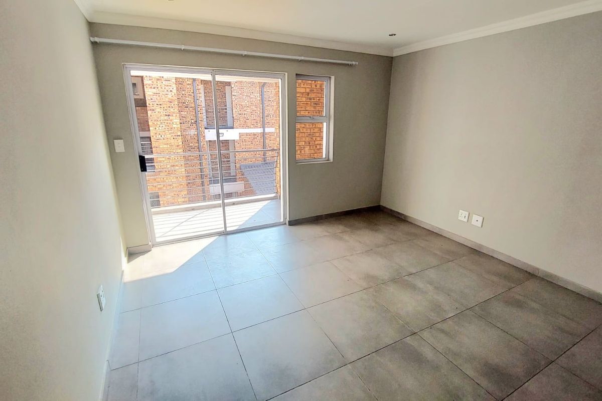 A bright, empty bedroom featuring large format floor tiles, neutral walls, and a sliding glass door providing access to a private balcony.
