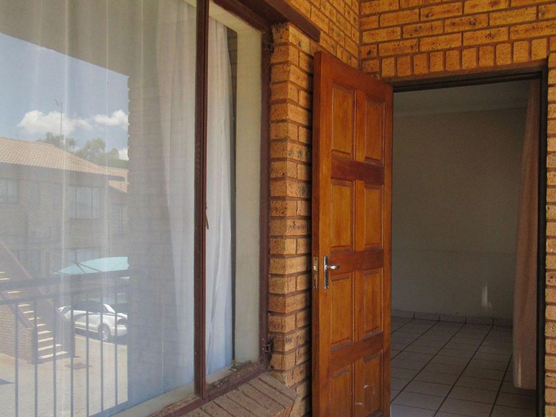 A view of a balcony entrance featuring face brick walls, a timber door, and tiled flooring, looking into an empty interior space.