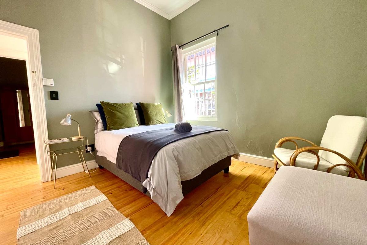 A bedroom featuring polished hardwood flooring, classic cornicing, and a sash window, with visible plaster cracking on the wall.