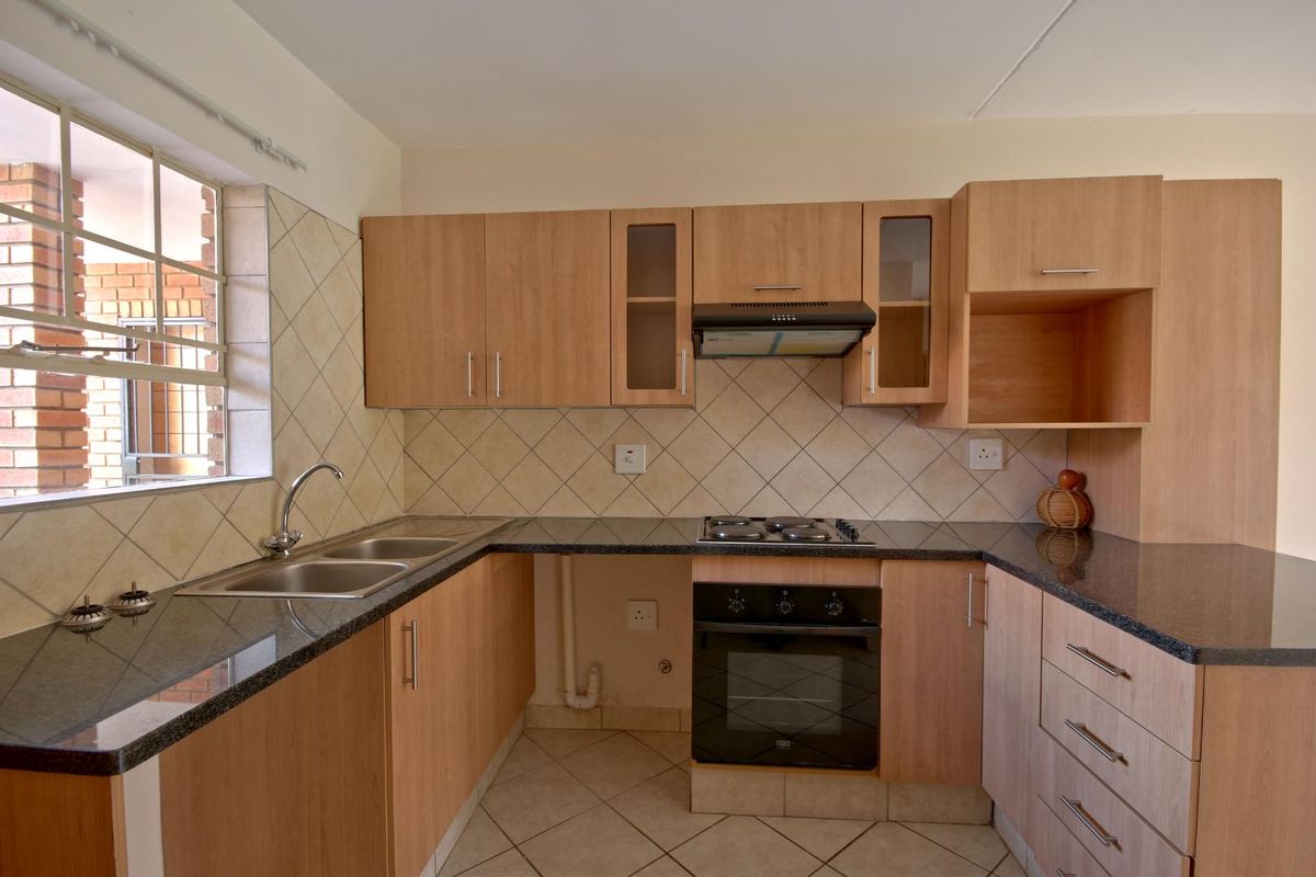 A functional kitchen featuring light wood cabinetry, granite countertops, a gas hob, built-in oven, and tiled backsplash with neutral flooring.