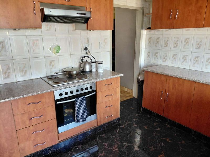 A functional kitchen featuring wood-look cabinetry, granite-style laminate countertops, built-in oven, electric hob, and extractor fan with tiled splashbacks.