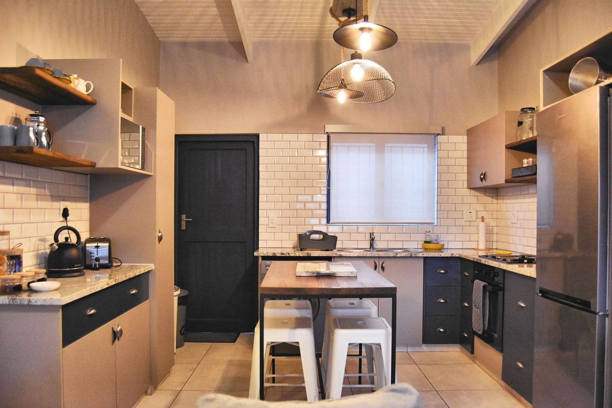 A modern kitchen featuring subway tile backsplash, stone countertops, built-in cabinetry, a central island, and exposed beam ceiling detail.