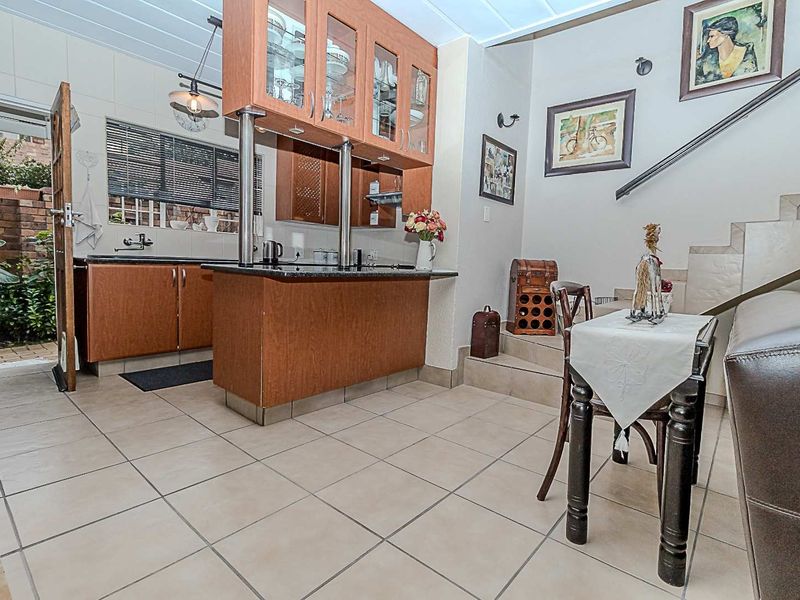 Open plan kitchen and dining area featuring tiled flooring, built-in wooden cabinetry with granite countertops, and an adjacent staircase with a metal handrail.