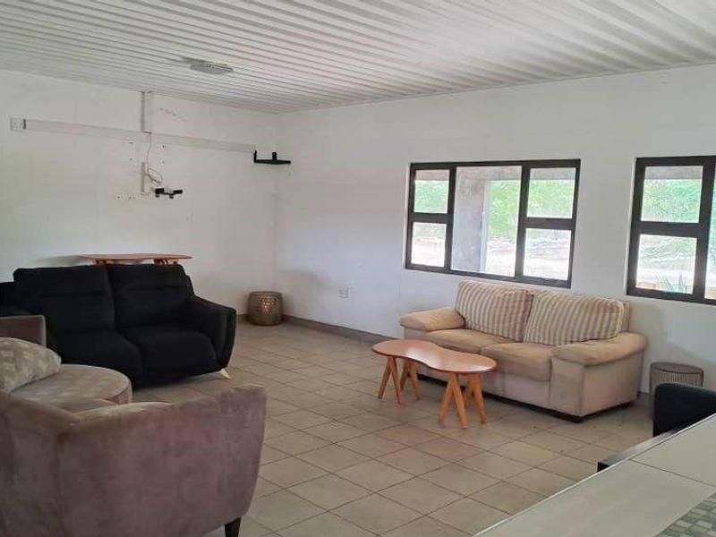 Spacious living area featuring tiled flooring, a corrugated metal ceiling, and large aluminium-framed windows, offering a blank canvas for interior updates.