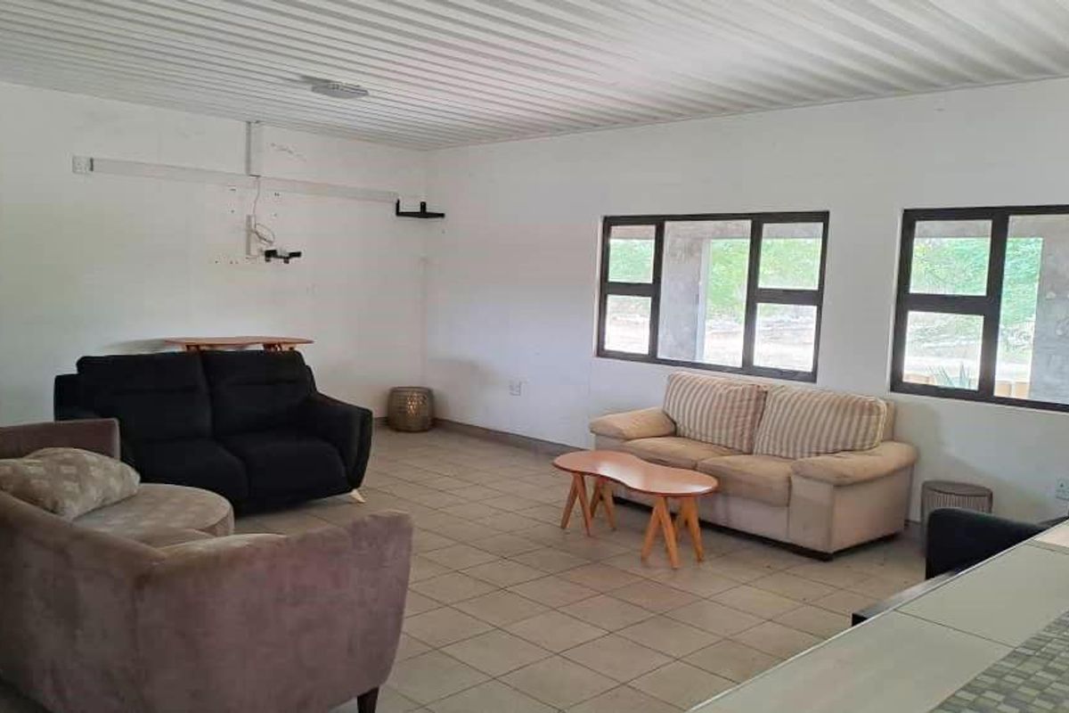 Spacious living area featuring tiled flooring, a corrugated metal ceiling, and large aluminium-framed windows, offering a blank canvas for interior updates.