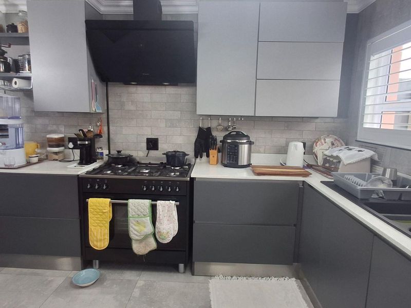 Modern kitchen featuring dark grey cabinetry, stone countertops, a gas stove with extractor fan, and a stylish subway tile backsplash.
