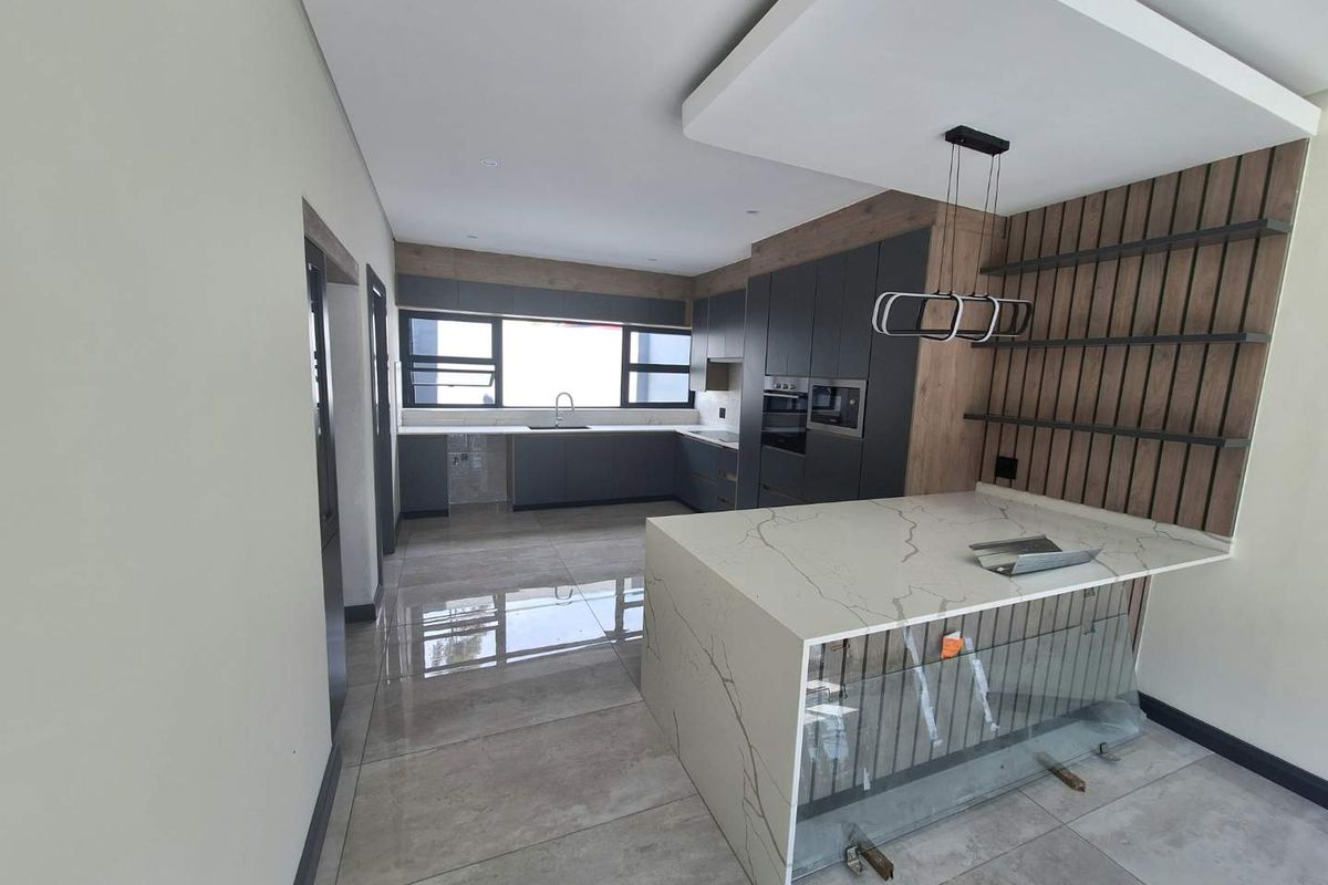 Modern kitchen featuring a quartz island, built-in appliances, and a stylish slatted wood feature wall with floating shelves, currently in the final stages of completion.