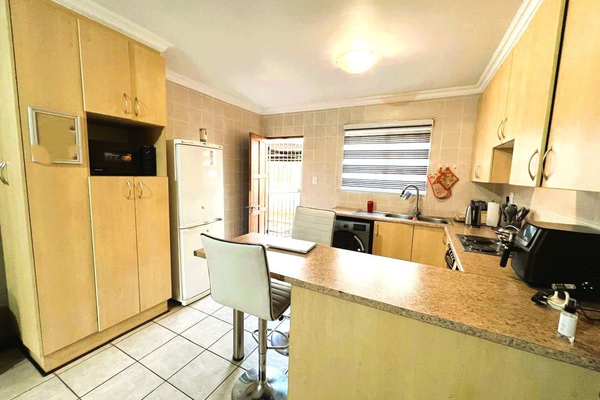 A functional kitchen featuring light wood-finish cabinetry, laminate countertops, tiled backsplash, and tiled flooring with direct access to an exterior area.