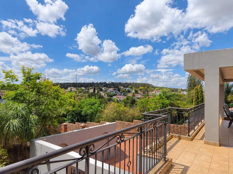 A spacious covered balcony featuring tiled flooring and a wrought iron balustrade, offering elevated views of the surrounding neighbourhood and lush greenery.