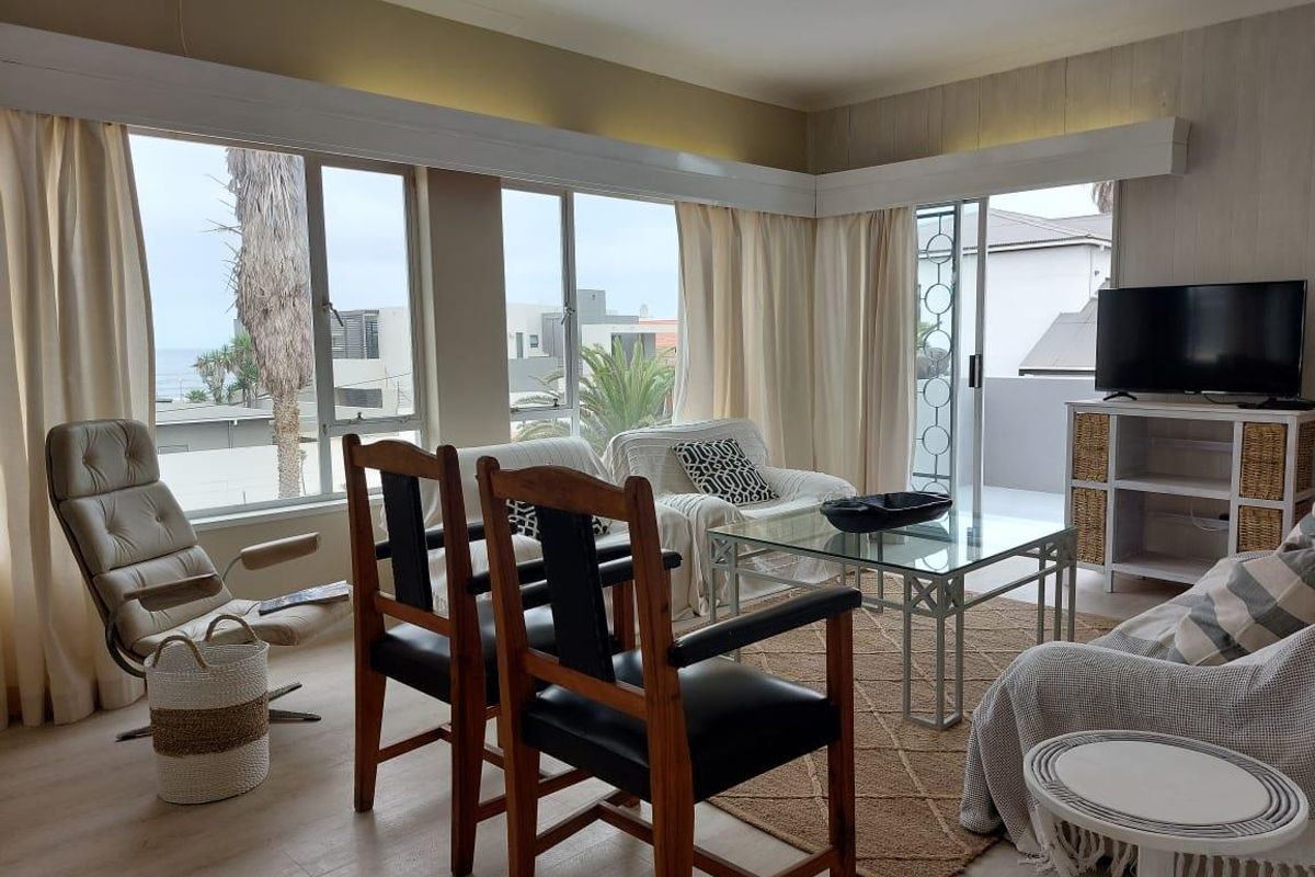 A bright living room featuring large windows with ocean views, integrated pelmet lighting, and direct access to an outdoor balcony area.