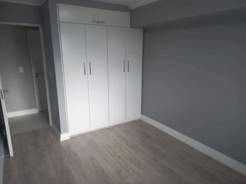 A clean, empty bedroom featuring modern grey laminate flooring, neutral grey walls, and white built-in cupboards with sleek handles.