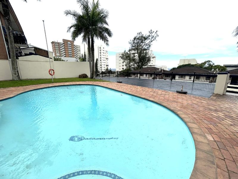 A communal swimming pool area featuring brick paving, a safety railing, and a pool cover, set within a residential complex.