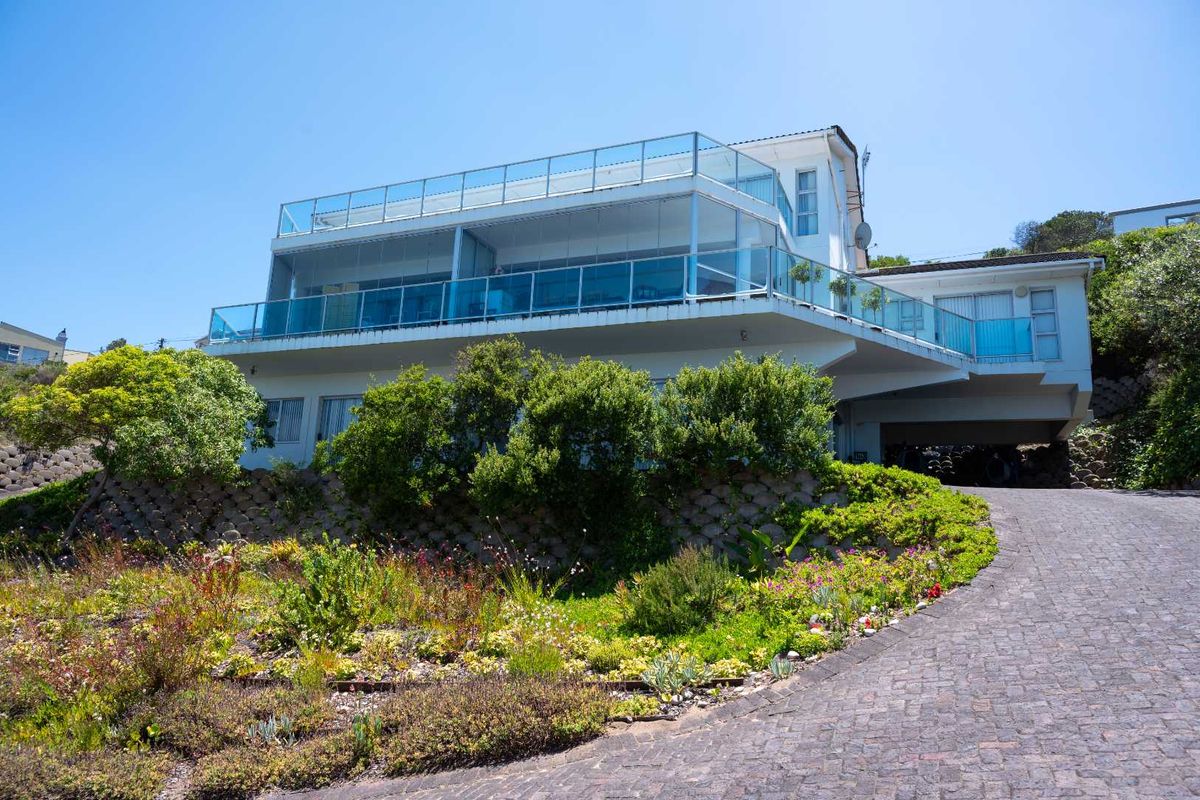A modern multi-level residence featuring expansive glass balconies, a paved driveway, and tiered landscaped gardens.