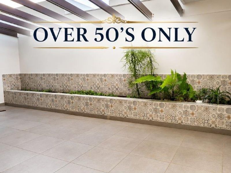A covered patio area featuring tiled flooring, a built-in decorative planter box, and a pergola structure, providing a clean and low-maintenance outdoor space.
