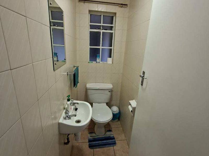 A compact bathroom featuring tiled walls and flooring, equipped with a wall-mounted basin and a standard toilet.