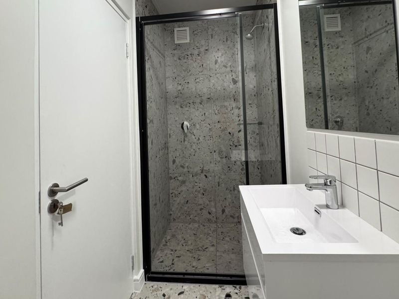 Modern bathroom featuring a walk-in shower with black-framed glass, terrazzo-style tiling, and a sleek white vanity basin with chrome fixtures.