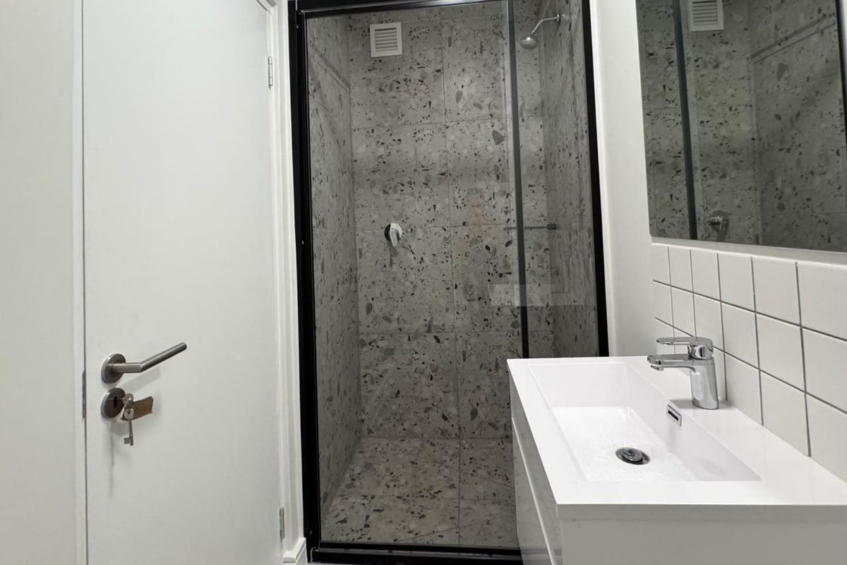 Modern bathroom featuring a walk-in shower with black-framed glass, terrazzo-style tiling, and a sleek white vanity basin with chrome fixtures.