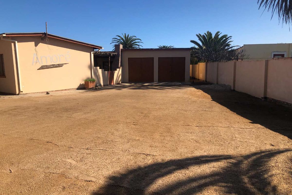 Spacious rear yard area featuring a double garage, perimeter walling, and an unpaved driveway surface with potential for landscaping or paving.