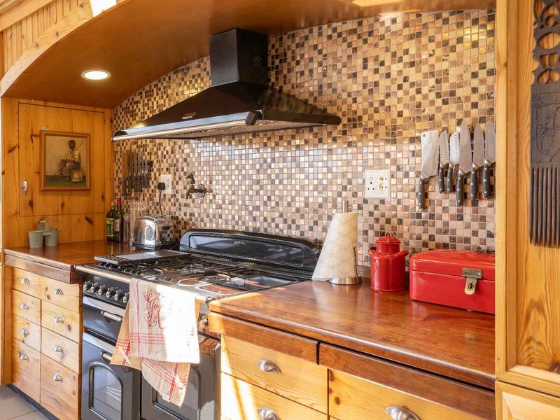 A rustic kitchen featuring warm wooden cabinetry, solid wood countertops, a mosaic tile backsplash, and a built-in gas stove with an extractor fan.