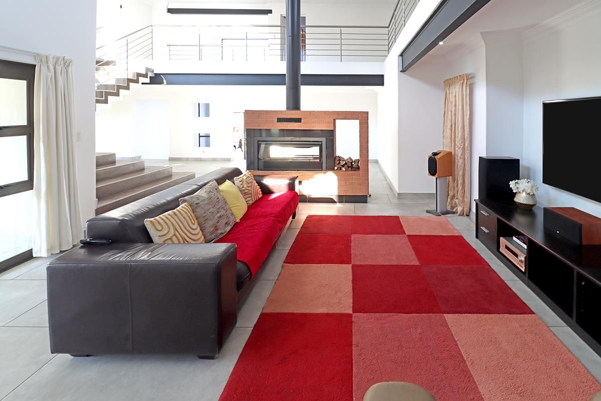 Spacious open-plan living area featuring a central brick fireplace, modern staircase, and mezzanine level with contemporary steel balustrades and tiled flooring.