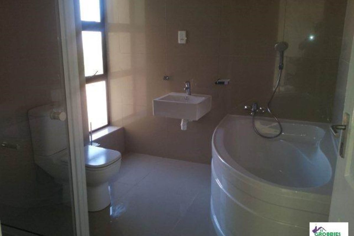 A modern bathroom featuring a corner bathtub, wall-mounted basin, and toilet with neutral floor-to-ceiling tiling.