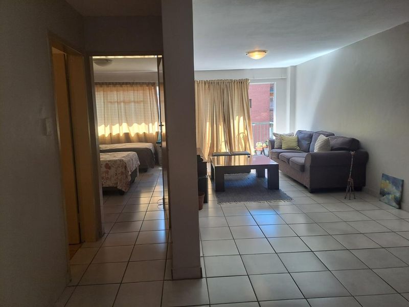 Open plan living area with tiled flooring and access to a balcony, connecting to an adjacent bedroom space.