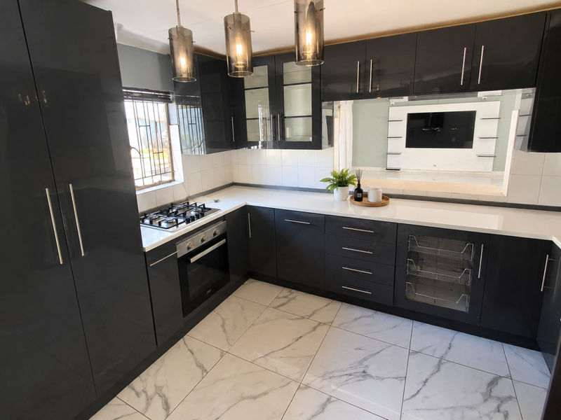 Modern kitchen featuring high-gloss dark cabinetry, white quartz countertops, built-in gas hob and oven, and elegant marble-look floor tiles.