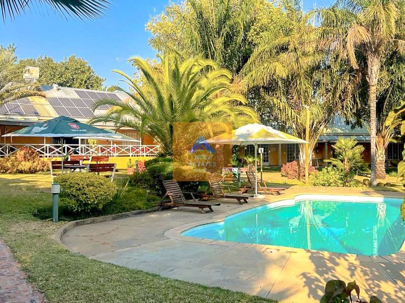 Outdoor pool area featuring a swimming pool, paved surround, and landscaped garden with solar panels installed on the adjacent building roof.