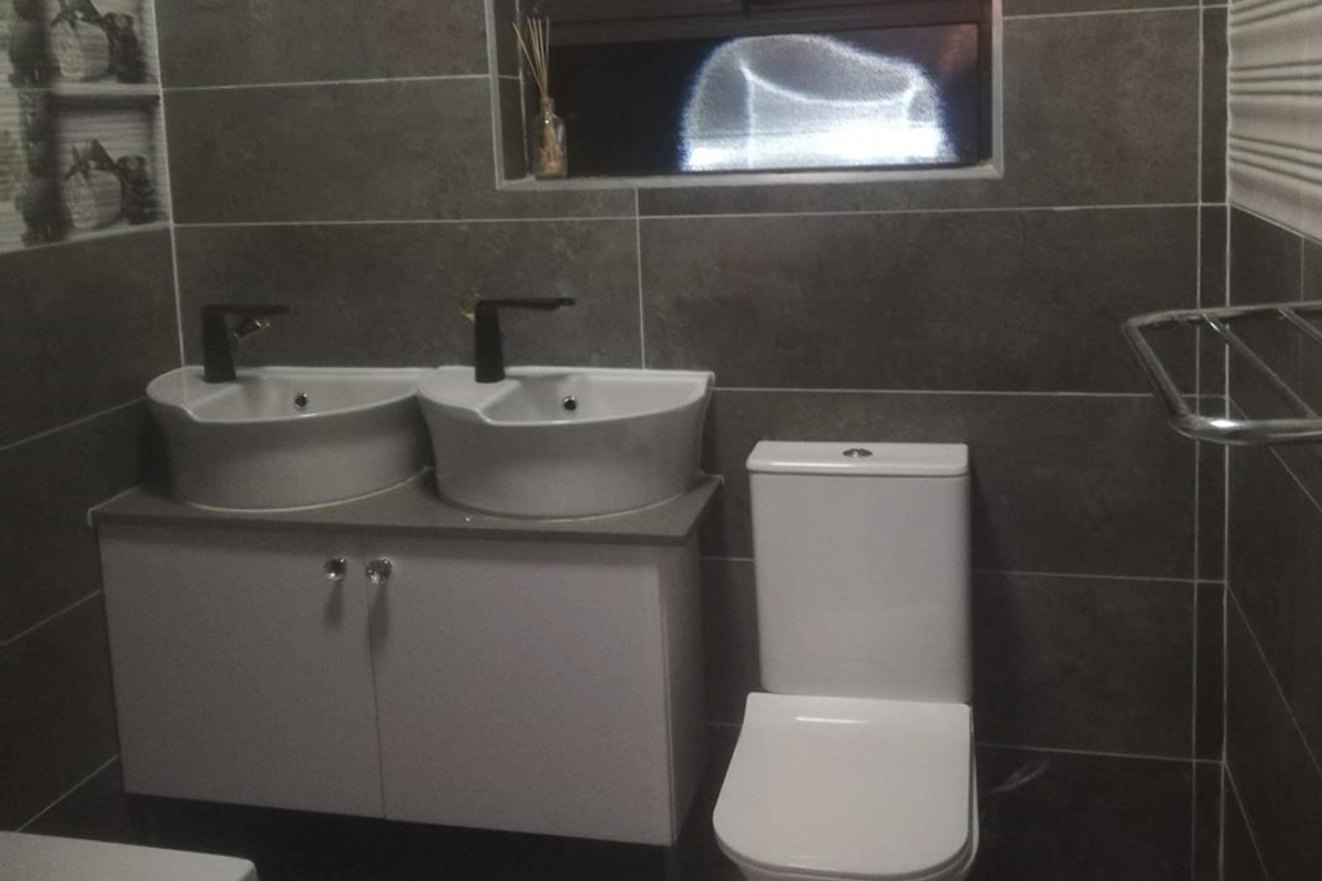 Modern bathroom featuring a double vanity with vessel sinks, black fixtures, and a wall-mounted toilet, finished with contemporary dark grey wall tiles.