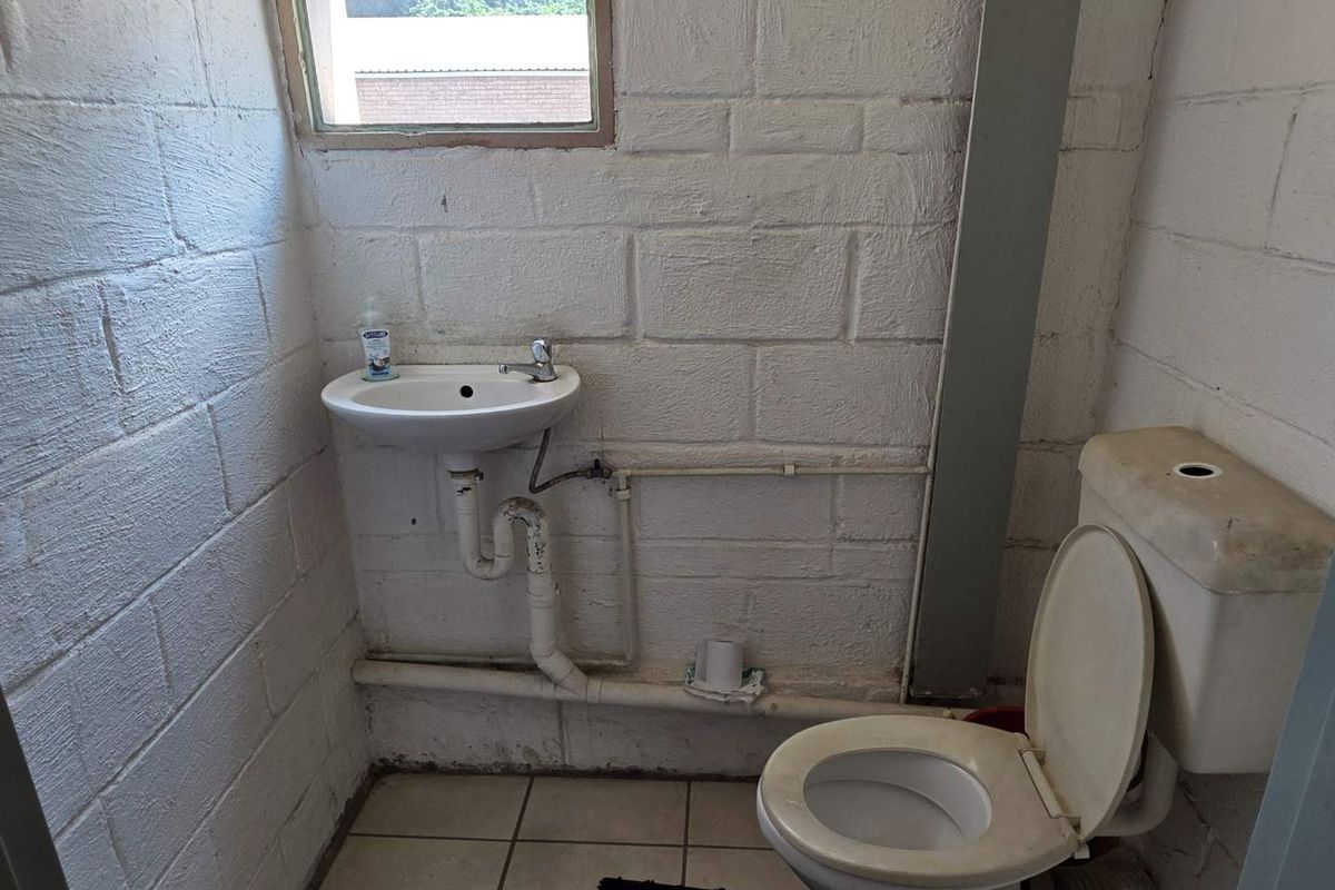 A basic industrial-style restroom featuring a wall-mounted basin and a standard toilet with exposed plumbing against painted concrete block walls.