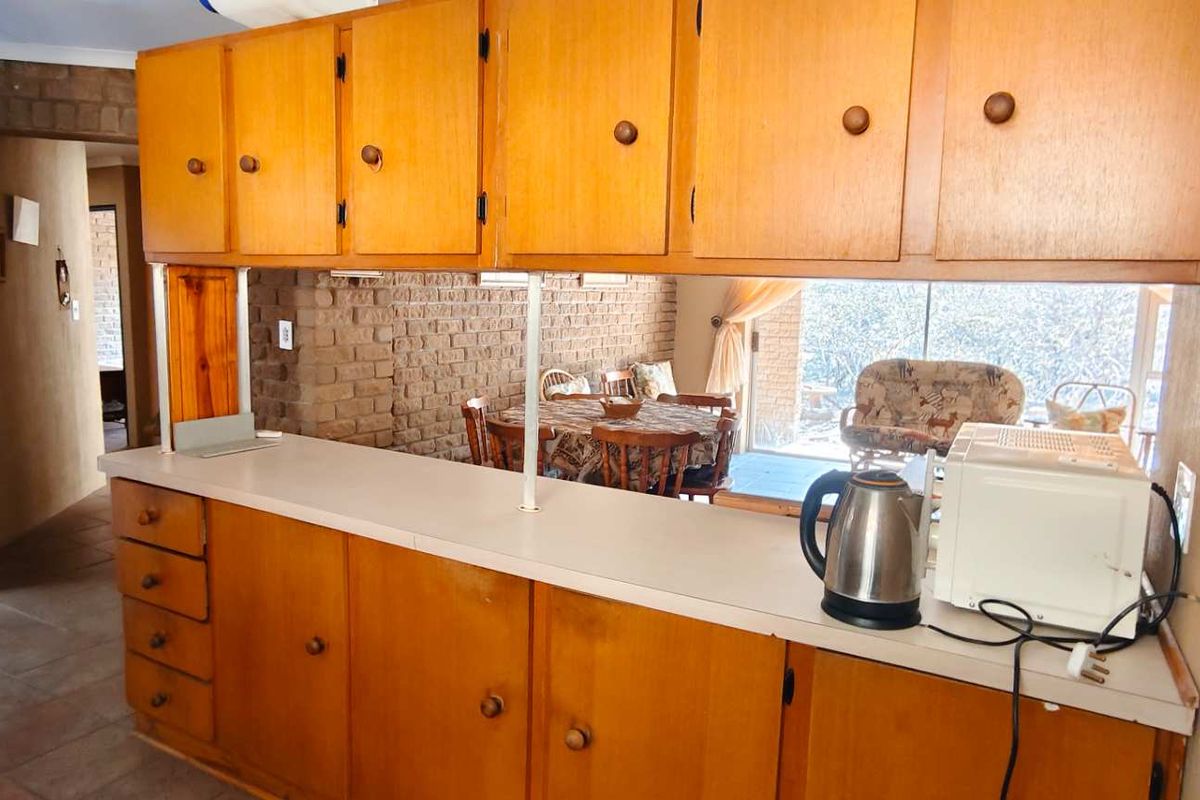 A dated kitchen area featuring wooden cabinetry and an exposed brick wall, offering a functional layout with a breakfast bar overlooking the dining space.