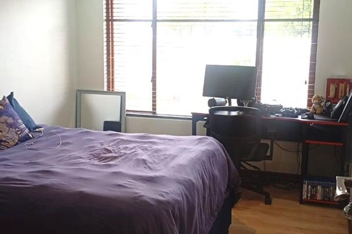 A well-lit bedroom featuring laminate flooring, decorative cornice, and a large window with fitted blinds, providing ample natural light.
