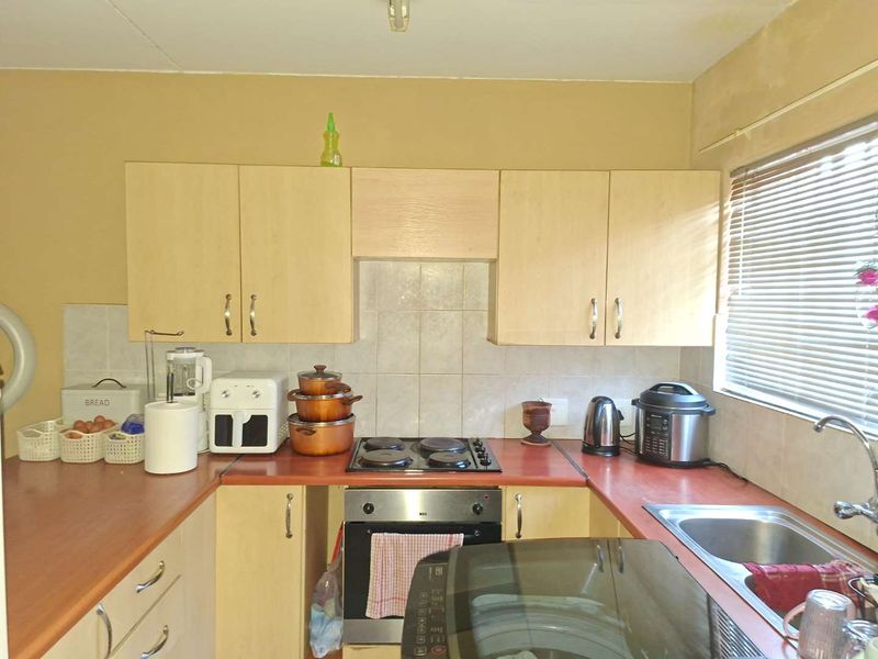 A functional kitchen featuring laminate cabinetry, built-in oven, electric hob, and a stainless steel sink with tiled splashback.