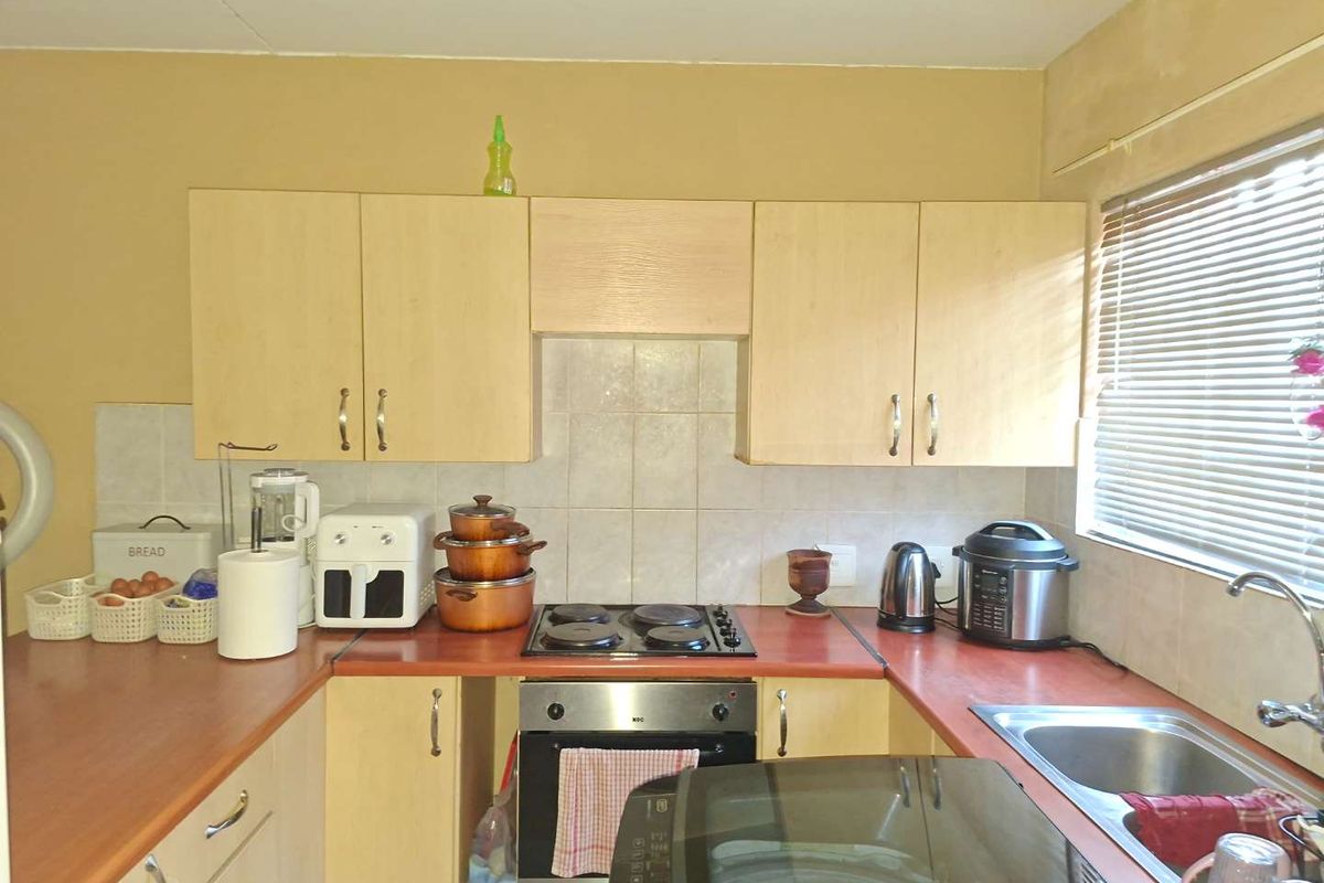 A functional kitchen featuring laminate cabinetry, built-in oven, electric hob, and a stainless steel sink with tiled splashback.