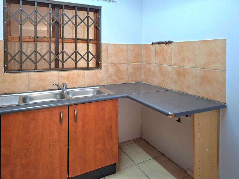 A compact kitchen area featuring a double stainless steel sink, laminate countertops, and tiled backsplash, currently awaiting updates to finishes and cabinetry.