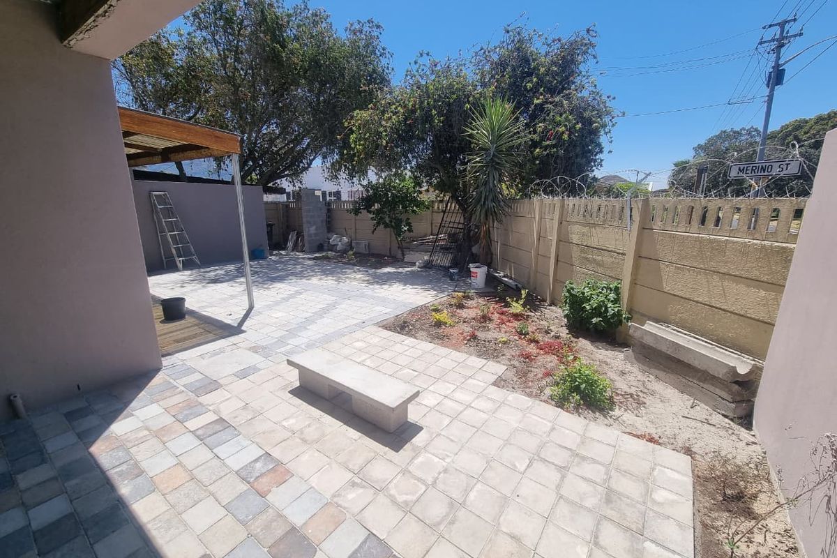 A rear outdoor area featuring a paved patio, a timber pergola, and a secure boundary wall with razor wire.