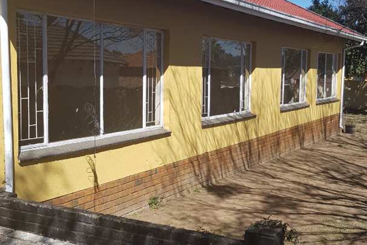 Rear view of the house featuring a tiled roof, yellow painted exterior walls with a brick plinth, and large windows with security bars.