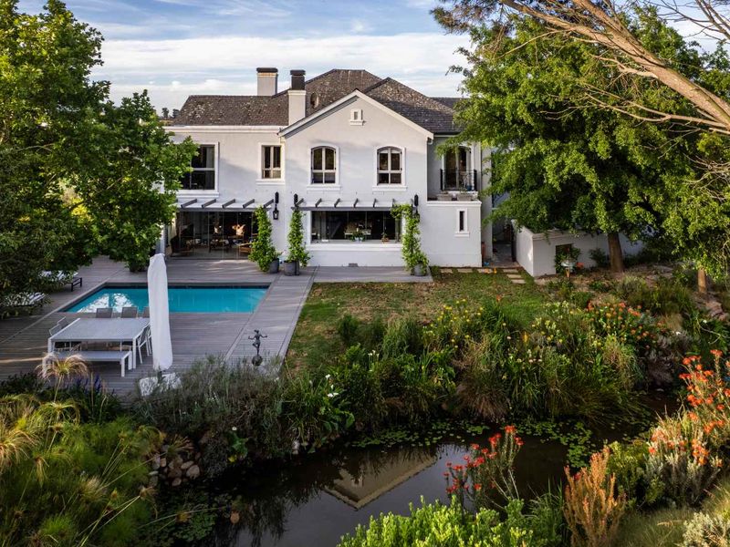 Rear view of a two-story residence featuring a swimming pool, timber decking, and a landscaped garden with a pond.